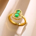 Nahaufnahme des goldenen Kalebasse-Rings mit grünen Edelsteinen auf weichem Stoff - Kürbis Grüner Stein / Gold-Grün