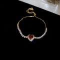 Macro shot of gold heart bracelet with red zircon and white stones on black background - Gold-Red Zirconia