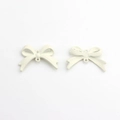 Detailed macro view of matte cream alloy bow charms with dual loops for DIY jewelry making - White