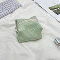 Close-up of mint green makeup bag featuring embossed heart patterns and white zipper - Green