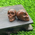 Carved red natural stone crystal skull pair with green spots on wooden base - Red Sesame