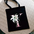 Black canvas tote bag with pink letter Y and white lily print on a textured background - Letter Y / Black