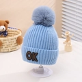 Detail of light blue knit kids hat with thick grey faux fur pompom and OK badge - One Size (2-5 Years) / Blue