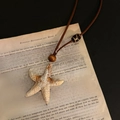 Macro d'un pendentif étoile de mer avec cordon marron sur de vieilles pages de livre - 15# Collier-Café-Géométrique (Style Étoile de Mer)