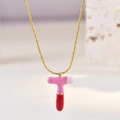 Macro detail of T-shaped gold necklace pendant with pink and white enamel drip finish - Letter T