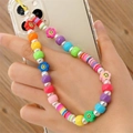 Bunte Perlen-Handykette mit Smile-Anhängern und Perlen auf einem Holzgrund - Mehrfarbiges Smiley-Gesicht Künstliche Perle