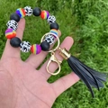 Close-up of silicone beaded keychain bracelet with cow print and tassel on grass - Black Cow Rainbow Style