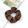 Detail of a brown satin scrunchie showing glossy texture and soft pleats on a magazine - Coffee