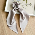 Detailed view of silver satin scrunchie with long ribbons on a wooden surface - Khaki