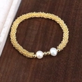 Elegantes Perlenarmband mit goldenen Perlen und zwei weißen Perlen auf Holzgrund - Gold