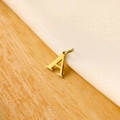 Detailed close-up of a golden A-shaped alphabet pendant on a textured wood and fabric surface - 14k Letter - A (letter Height 1cm)