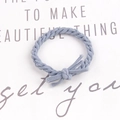 Detail of a braided misty blue elastic hair tie with a knot, shown on a clean paper background - Light Blue