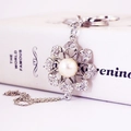 Silver flower keychain with central pearl and rhinestones resting on a white book - Silver