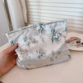 Dettaglio della trama floreale jacquard vintage su una borsa per cosmetici in seta premium - Azzurro