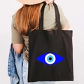 Black canvas tote bag with blue graffiti evil eye print shown on a model's shoulder - Design N-Blue Pupil Eye-Black