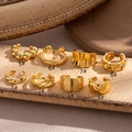 Set de ocho ear cuffs dorados con diversas texturas sobre una losa de piedra beige - Diseño de Cuentas (1#) / Oro