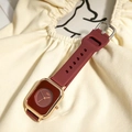 Detail view of square women's quartz watch with burgundy dial and gold case on beige fabric - Red