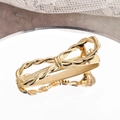 Golden twisted metal bow hair clip with spring clip design on a reflective mirror surface - Gold
