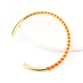 Detail of gold-plated open bangle with orange enamel segments on a white stand - Orange