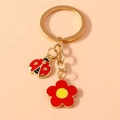 Vue détaillée de breloques coccinelle et fleur sur un porte-clés doré fond rose - Rouge
