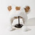 Dettaglio del cappello di peluche bianco con paraorecchie, macchie marroni e pompon - M (56-58cm) / Bianco
