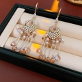 Detalle de pendientes dorados con borlas, perlas, cristales y cuentas de color ámbar - Colorido