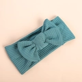 Detail shot of a dark green ribbed knit baby headband with a large bow on a pink surface - Dark Green
