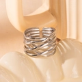 Detalle de anillo abierto plateado con textura de metal trenzado sobre fondo beige suave - Estilo de Envoltura Tejida (#0444)