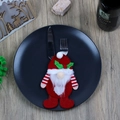 Kerstkabouter bestekhouder in rood en wit vilt op een zwart dinerbord - Rode Hoed Kabouter Bestekhouder