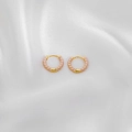 Detailansicht der goldenen Huggie-Creolen mit rosa Emaille-Spiralen auf weißer Seide - Rosa