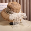 Close-up of an elegant straw hat featuring a white lace bow and delicate pearl trim - Khaki