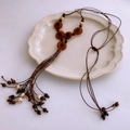Detailed close-up of ethnic beaded necklace featuring red resin pendants and tassels - Brown