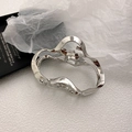 Detail of silver irregular wavy metal hair claw clip on a minimalist textured surface - Irregular Wave Design / Silver