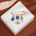 Detail of gold evil eye brooch with tassel charms on a white jewelry cushion - Multi-Eye Pendant Style (Z234)