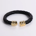 Macro detail of twisted black stainless steel cable with polished gold accents on cuff - Black + Gold