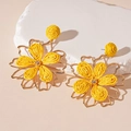 Detailed macro view of woven raffia petals and gold-tone frame on flower earrings - Yellow