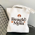 Cream canvas tote bag featuring Beagle Mom artistic print and dog illustration on a black chair - Beagle Mom Script