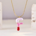 Macro shot of letter F pendant with pink and white enamel detail on golden chain - Letter F