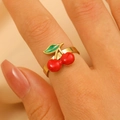 Elegante anello dorato con ciliegie rosse e foglie verdi indossato da modella - Anello a Ciliegia in Acciaio Inossidabile (X760)