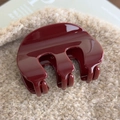 Detail of dark red acrylic hair claw clip with glossy finish on soft beige plush fabric - Red