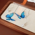 Detailaufnahme von Schmetterlingsohrringen mit blauen Flügeln und Perlen auf Holztablett - Blaue Schmetterlings-Perlen-Ohrfäden
