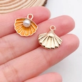 Golden scallop pendant with orange enamel and faux pearl on a finger for DIY jewelry - Shell