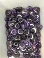 Close-up of polished amethyst heart stones piled in a white bowl with natural texture - Purple Crystal