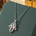 Silver Hamsa Hand necklace with blue Evil Eye and heart charms on a green jewelry box - A10-Silver