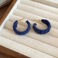 Close-up of navy blue velvet C-shaped hoop earrings with gold metal on a beige tray - Blue