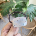Nahaufnahme von cremefarbenem Haargummi mit bunten Strasssteinen und braunem Gummiband - Weißes Perlmutt