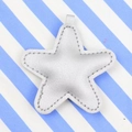 Silver star-shaped leather pendant with lychee texture on blue striped fabric background - Silver