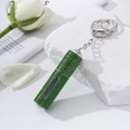Detail of green rhinestone perfume atomizer keychain next to white roses and stones - Green