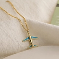 Macro d'un collier pendentif avion doré avec émail bleu sur un tissu doux crème - Avion Bleu