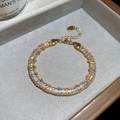 Gros plan d'un bracelet chaîne doré orné de strass sur un plateau à bijoux gris - Doré